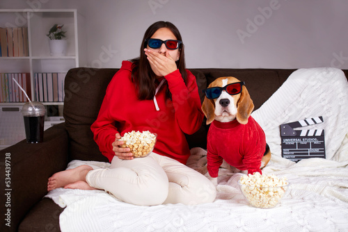 A young girl with her dog beagle in 3 d glasses watching a movie at home, eating popcorn.  photo