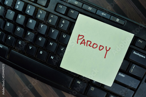 Concept of Parody write on sticky notes with keyboard computer isolated on Wooden Table.