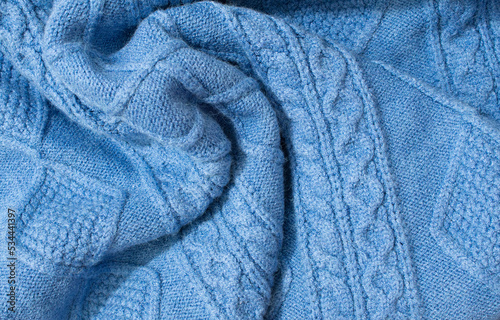 Blue warm knitted sweater with a pattern. Blue woolen sweater, knitted sweater texture, knitted background. Blue knitted textured background with a pattern closeup