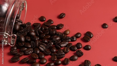 Glass Jar with Roasted Coffee beans falling down on pink close up