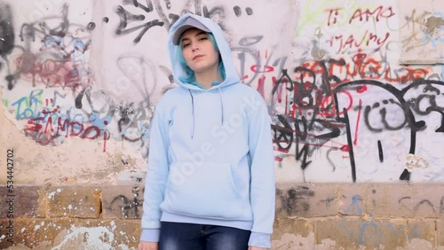Teenager in light blue oversize hoodie and jeans. Blue haired teen girl stays outdoor against graffiti wall. Clothing mockup