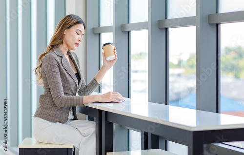 Millennial Asian successful professional female businesswoman in formal suit take break sitting smiling browsing surfing internet via tablet computer and drinking coffee from disposable cup in office Free Download Millennial Asian successful professional female businesswoman in formal suit take break sitting smiling browsing surfing internet via tablet computer and drinking coffee from disposable cup in office - GFXLoad