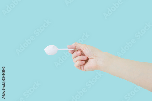 Dry collagen powder in a measuring spoon  hand. Nutritional supplements. Blue background.