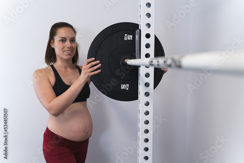 Pregnant woman placing weights on a barbell in a squat rack in a home gym