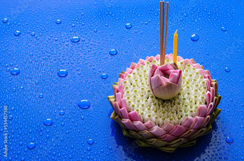 Pink lotus petal krathong for Thailand Loy Krathong festival decorates with its flower, crown flower, incense stick and candle on blue background with water drop.