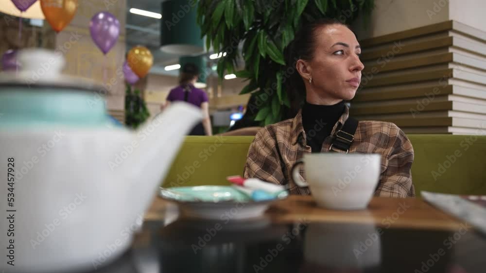 Young beautiful woman sitting in restaurant and thoughtfully drinking delicious drink from mug. Holiday in cafe with balloons. Teapot with delicious tea. Leisure indoor. Hands holding coffee mug. Young beautiful woman sitting in restaurant and thoughtfully drinking delicious drink from mug. Holiday in cafe with balloons. Teapot with delicious tea. Leisure indoor. Hands holding coffee mug.