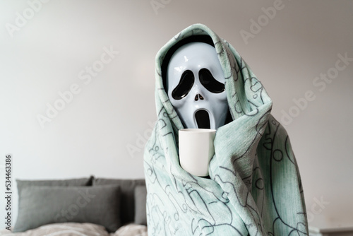 Unrecognised person in ghost sad mask in plaid freezing at home. Cold Halloween at home. Energy crisis 