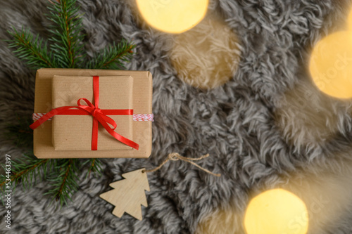 Christmas present boxes with different ribbons on a cosy gray blanket with pine branches, wooden Christmas tree decoration and fairy lights photo