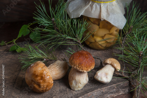 Three porcini mushrooms commonly known as Boletus Edulis and glass jar with canned mushrooms on vintage wooden background..