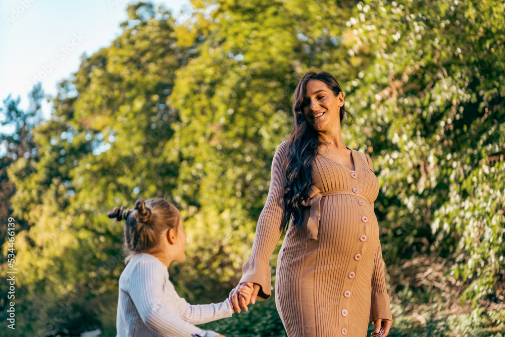 A pregnant woman and her daughter are walking in the park in the fall. they are enjoying the good weather and fresh air. A pregnant woman and her daughter are walking in the park in the fall. they are enjoying the good weather and fresh air.