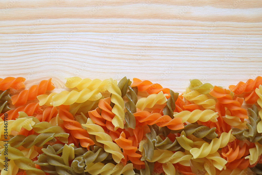 Heap of Vegeroni spiral shaped three-color fusilli pasta on wooden background Heap of Vegeroni spiral shaped three-color fusilli pasta on wooden background