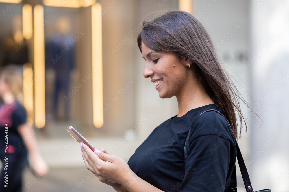 Beautiful smiling woman in black shirt texting on smartphone on street in city center Beautiful smiling woman in black shirt texting on smartphone on street in city center