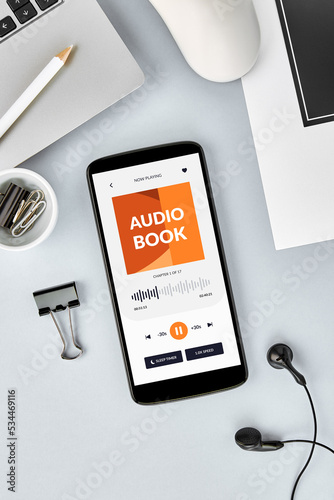 Vertical overhead view of smartphone screen with audio book app open on desk. 