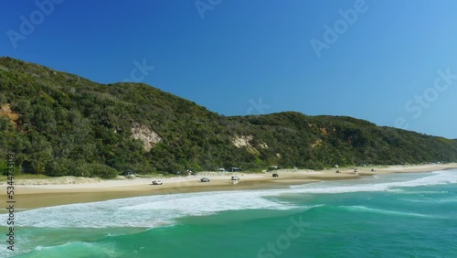 4WD Cars Driving Along Sandy Beach Shore Beside Blue Ocean Waves In Australia, 4K Aerial Drone photo