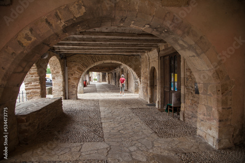 Fotografie, Obraz Touriste solitaire promenant sous les arcades du villde de sauveterre de Rouergu