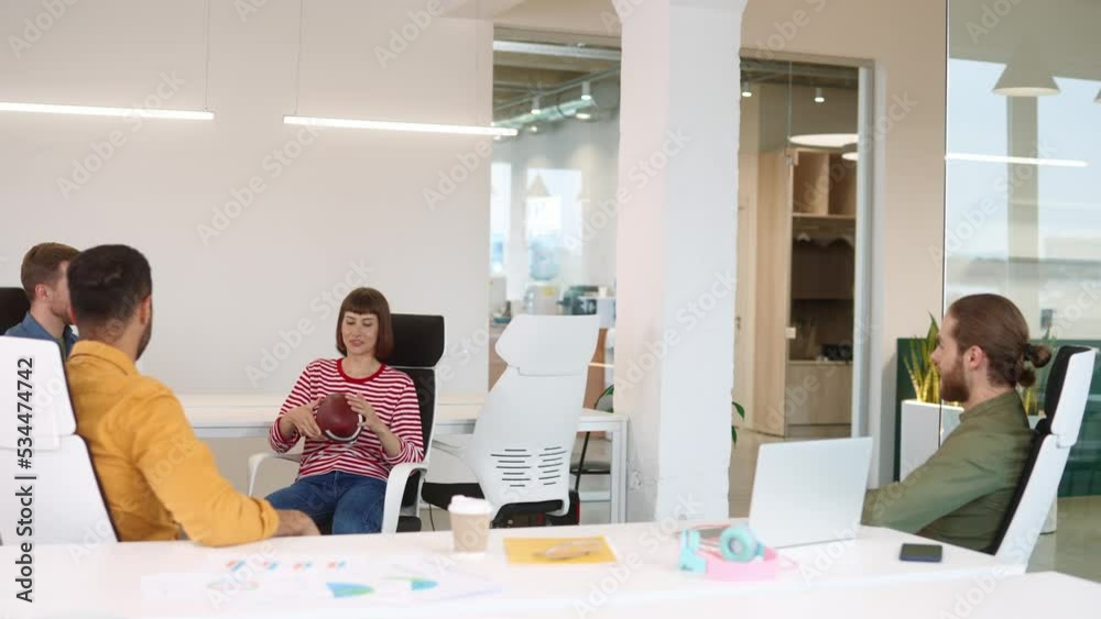 Young team of casual modern professionals sitting indoor in light office and throwing baseball having fun during workday. Group of multi-ethnic workers playing with ball in cabinet. Team building Young team of casual modern professionals sitting indoor in light office and throwing baseball having fun during workday. Group of multi-ethnic workers playing with ball in cabinet. Team building