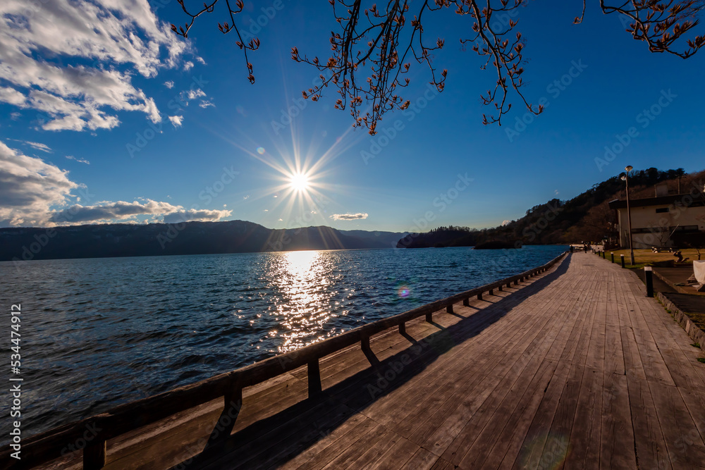 春の青森県・十和田湖で見た、夕暮れに差し掛かる時間の太陽と快晴の青空