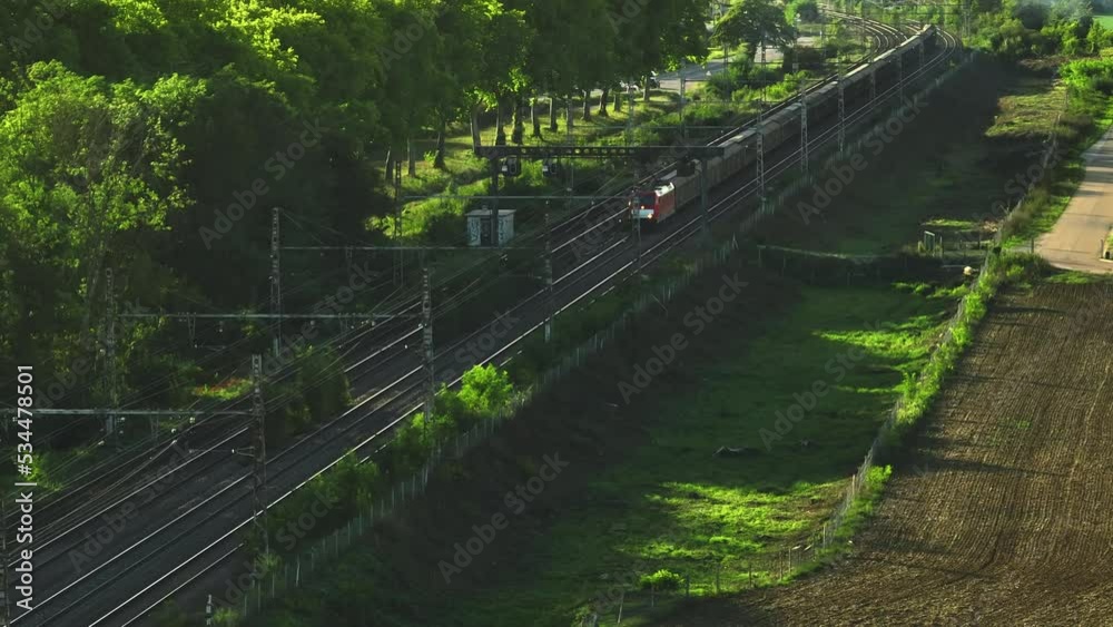 Aerial view of fast passenger train driving on railroad. High angle view of passing high speed train in rural summer country landscape. Train movement aerial view, parallax effect.
