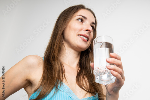 Smiling young woman holding a glass of water on a white background. Top view, flat lay