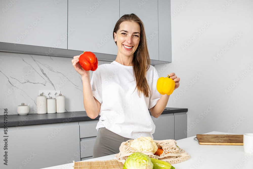 Fototapeta premium Smiling young woman laying out purchases from the store in the kitchen