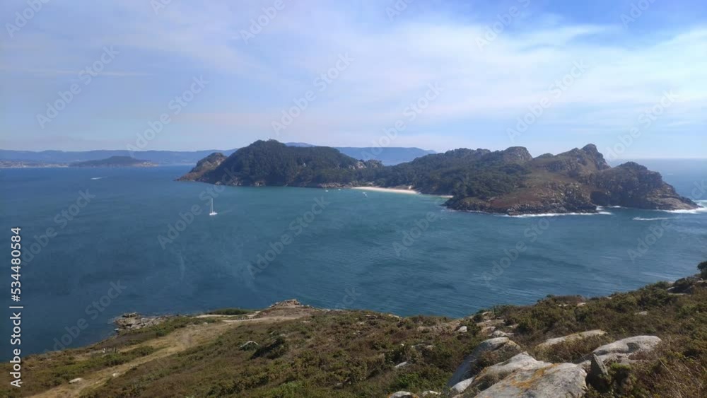 mountainous island with beach and sailboat sailing in front on a sunny day, panoramic shot roll to the right, Cíes island, Pontevedra, Galicia, Spain mountainous island with beach and sailboat sailing in front on a sunny day, panoramic shot roll to the right, Cíes island, Pontevedra, Galicia, Spain
