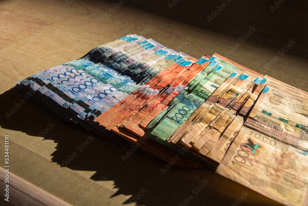 Tenge currency of different denominations lie on the table. A pack of tenge is scattered on the table