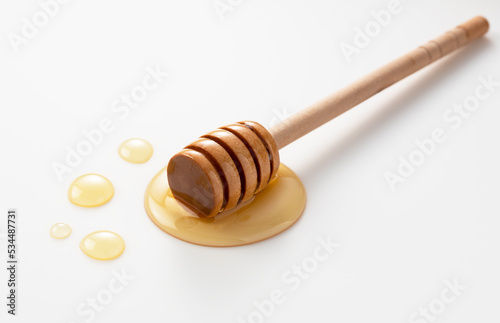 Wooden honey dipper with honey on white background.