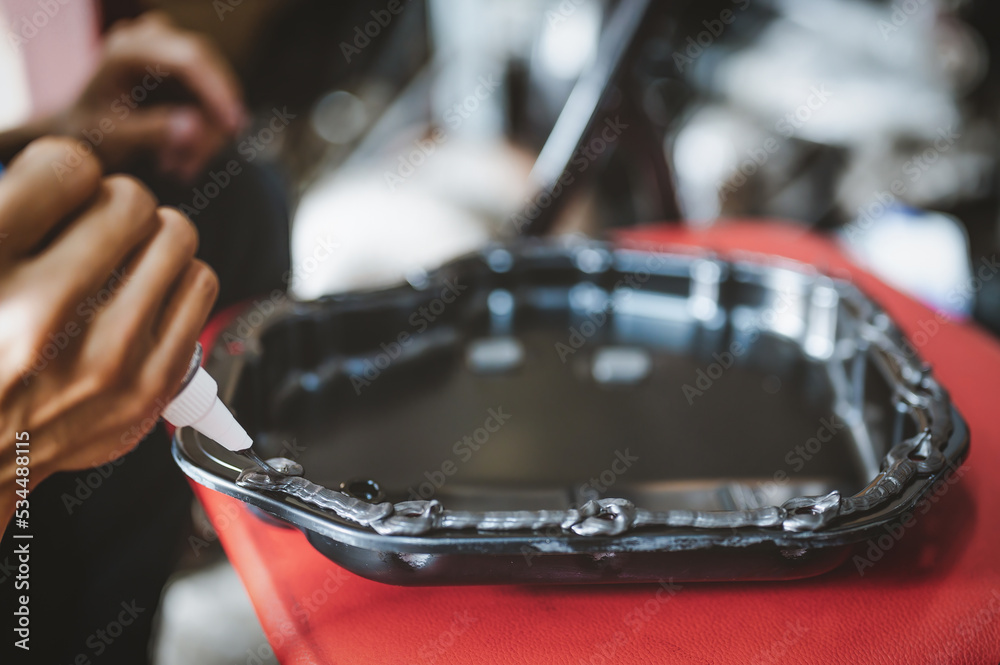 Auto mechanic applying black hightemp RTV silicone gasket maker to oil