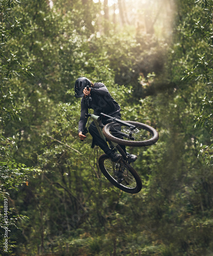 Cycling, bicycle jump and sports man travel in Japan nature forest for adventure and extreme sport journey. Trees, stunt and mountain bike rider or cyclist training in woods for exercise and fitness