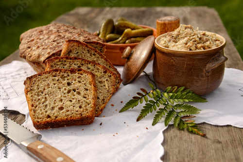 Wiejski stół — bochenek chleba pokrojony w kromki, ogórki kiszone i smalec domowej roboty © Anna