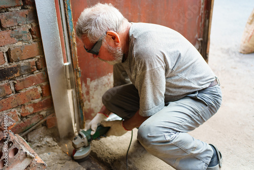 elderly gray-haired man in gloves cleans the metal structure from rust. 