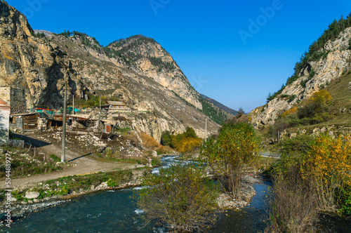 Autumn landscape in the mountains. Yellowed trees in autumn in the mountains of North Ossetia. Mountain gorges. View of the mountain peaks. A village in the mountains and a mountain river. © Eduard Belkin