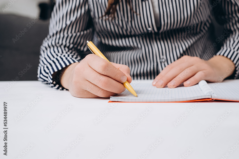 Close up of female hands writing in notepad placed on white wooden desktop with copy space for promotion content. Businesswoman writes startup business ideas and plans, creative thoughts to notebook Close up of female hands writing in notepad placed on white wooden desktop with copy space for promotion content. Businesswoman writes startup business ideas and plans, creative thoughts to notebook