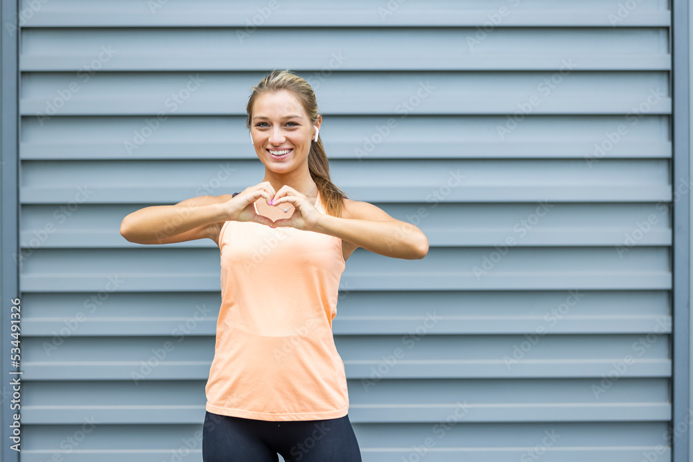 Portrait of smiling woman in sports clothing making a heart sign with her hands. Active woman making a heart with her hands. Beautiful middle aged woman laughing after workout Portrait of smiling woman in sports clothing making a heart sign with her hands. Active woman making a heart with her hands. Beautiful middle aged woman laughing after workout