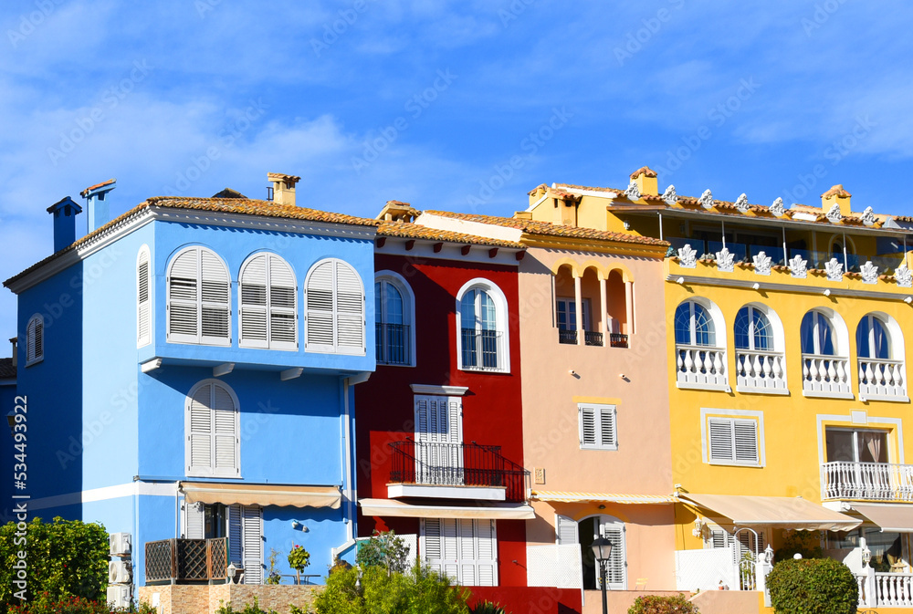 Fototapeta premium Yachts and motor boats in marina Port Saplaya, Valencia, Alboraya, Spain. Luxury yacht and fishing motorboat in yacht club on background of the colourful houses at Mediterranean Sea. Sailboat port.