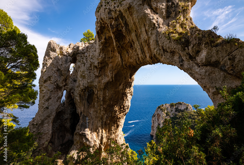 “Arco Naturale“ is a natural limestone arch that forms a bridge between two pillars of rock. It is located on the top of a cliff on Capri island Italy. Formation with mediterranean sea in background.