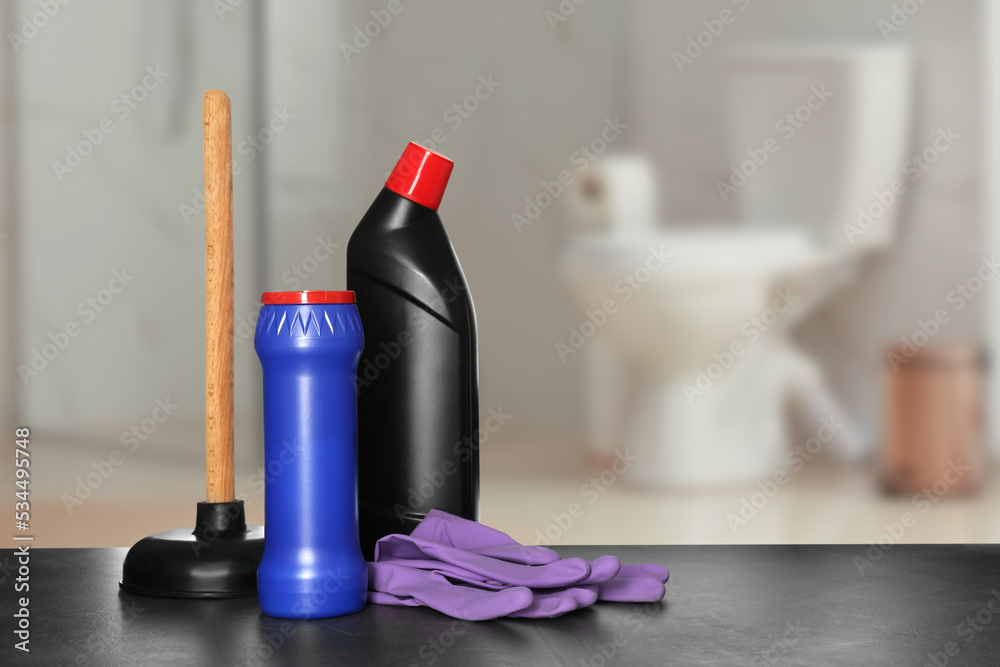 Different toilet cleaning supplies on black table in bathroom, space for text