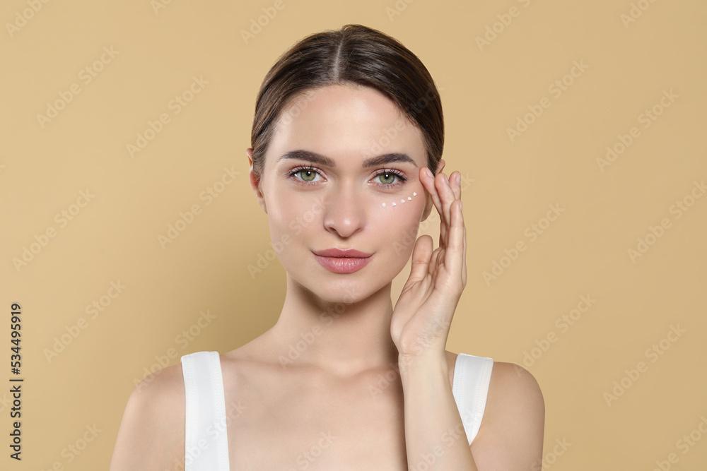 Young woman with cream around eye on beige background Young woman with cream around eye on beige background