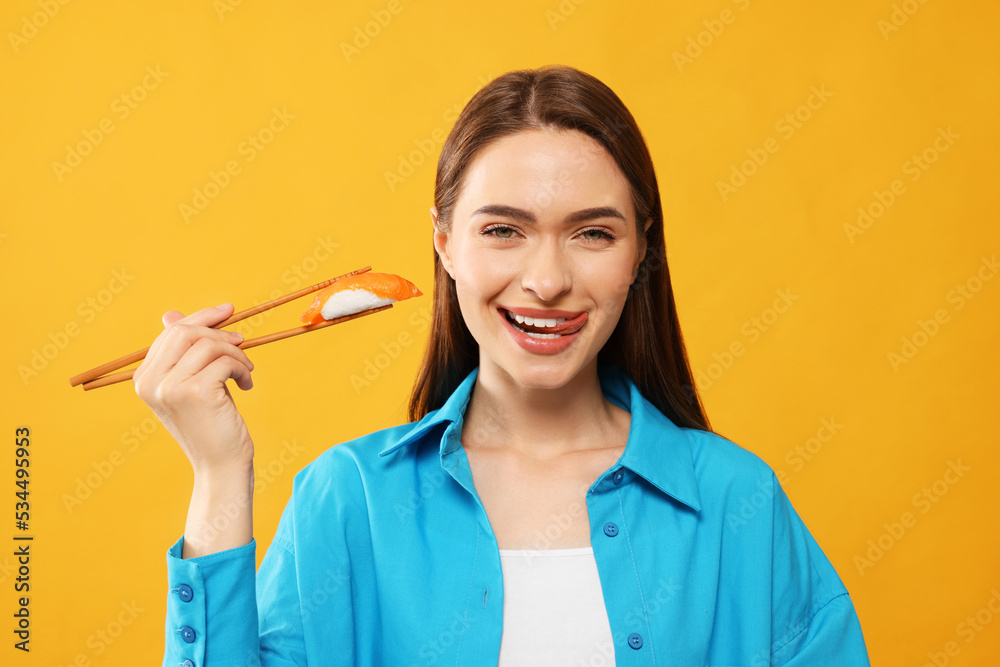 Happy beautiful young woman holding sushi with chopsticks on orange background Happy beautiful young woman holding sushi with chopsticks on orange background