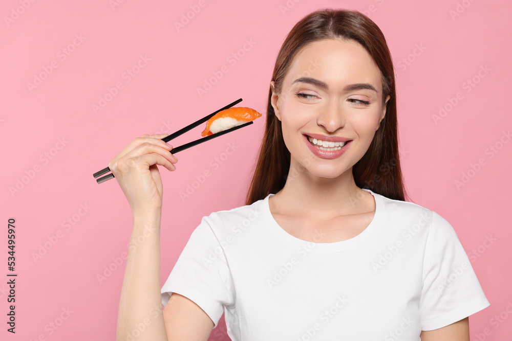Beautiful young woman holding sushi with chopsticks on pink background Beautiful young woman holding sushi with chopsticks on pink background