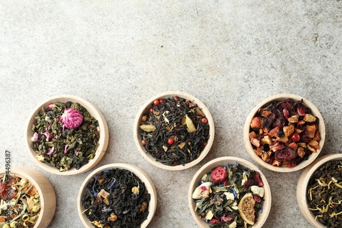 Different kinds of dry herbal tea in wooden bowls on light grey table  flat lay. Space for text