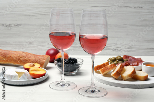 Glasses of delicious rose wine and snacks on white wooden table