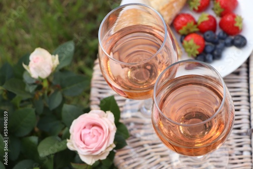 Flowers near glasses of delicious rose wine and food on picnic basket outdoors, closeup