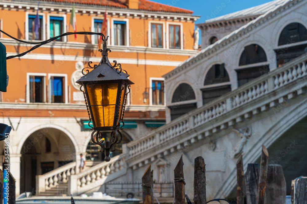 Antique street lighting lantern against the background of a vintage house and a bridge against the blue sky on the bank of the canal street of the city of Venice, Venetian street lamp