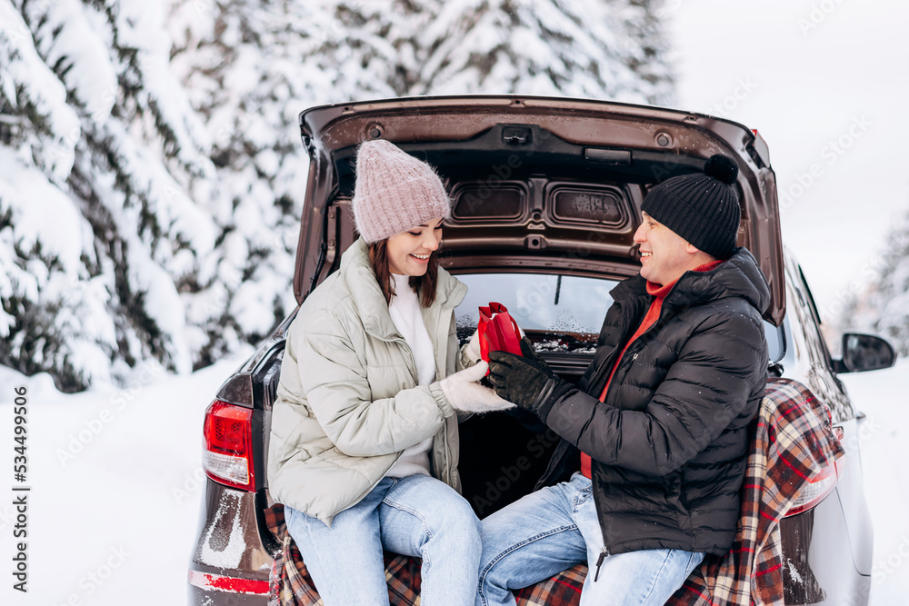 A young man in love gives a gift to a young woman in the open trunk of a car in a winter forest.Winter holidays,Valentine's day,tenderness and love.