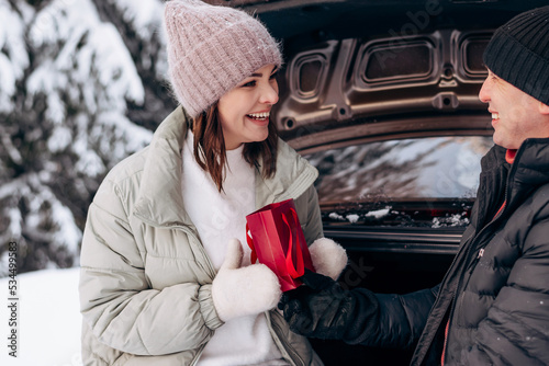 A young man in love gives a gift to a young woman in the open trunk of a car in a winter forest.Winter holidays,Valentine's day,tenderness and love. © Tatyana