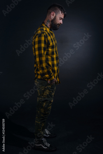 Profile portrait picture of a bearded man with tattoos on his face and neck in yellow black shirt © qunica.com