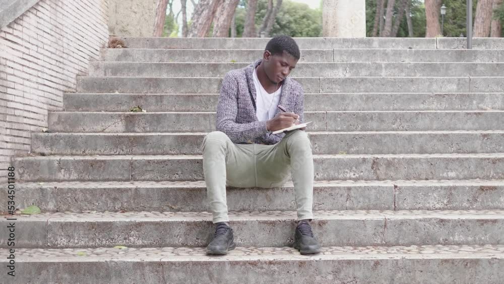 Peaceful african man writing notes on his agenda on the steps Peaceful african man writing notes on his agenda on the steps