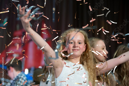 Happy face of a little girl in falling confetti. Magic Time - Portrait of a very happy child with hands smiling while confetti falls. For a children's party or birthday.