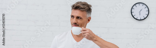 Man in t-shirt holding cup of coffee at home, banner.